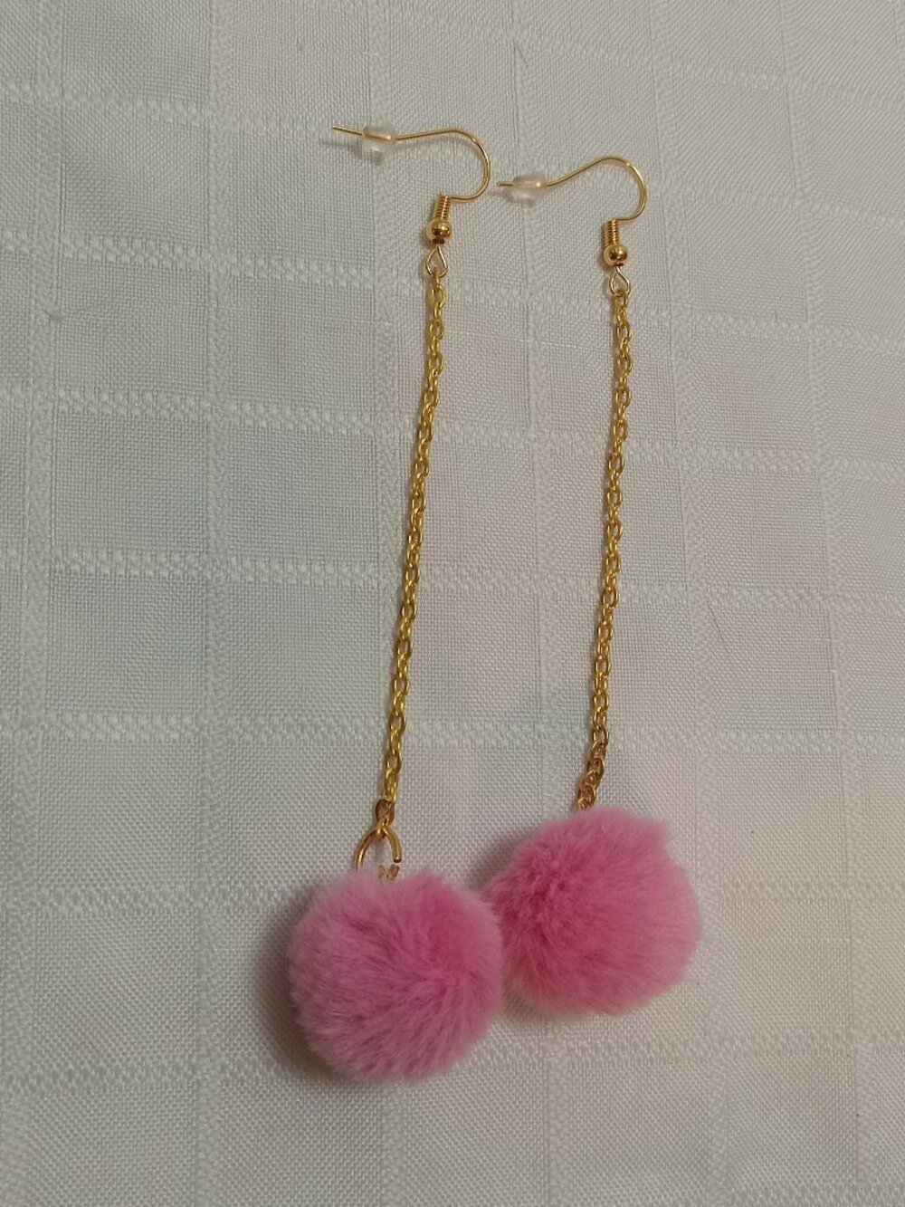 Handmade earrings with small pom-poms and gold-colored accent hooks and chains